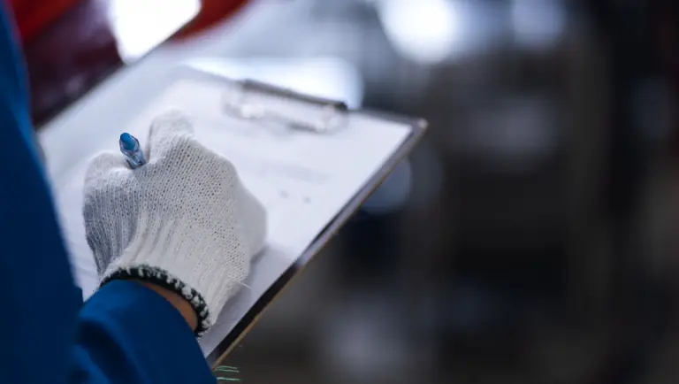 Person som bär skyddshandskar och fyller i en checklista eller ett formulär på en clipboard